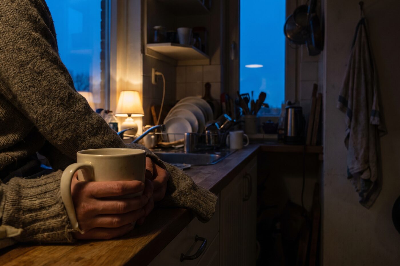 Iemand staat vroeg in de ochtend aan het aanrecht met beide handen om een mok