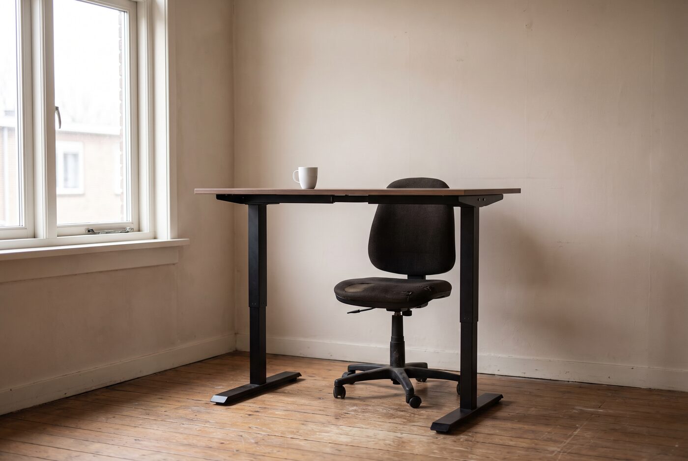Een sta-bureau op stahoogte met een bureaustoel eronder geschoven, in een werkkamer bij daglicht