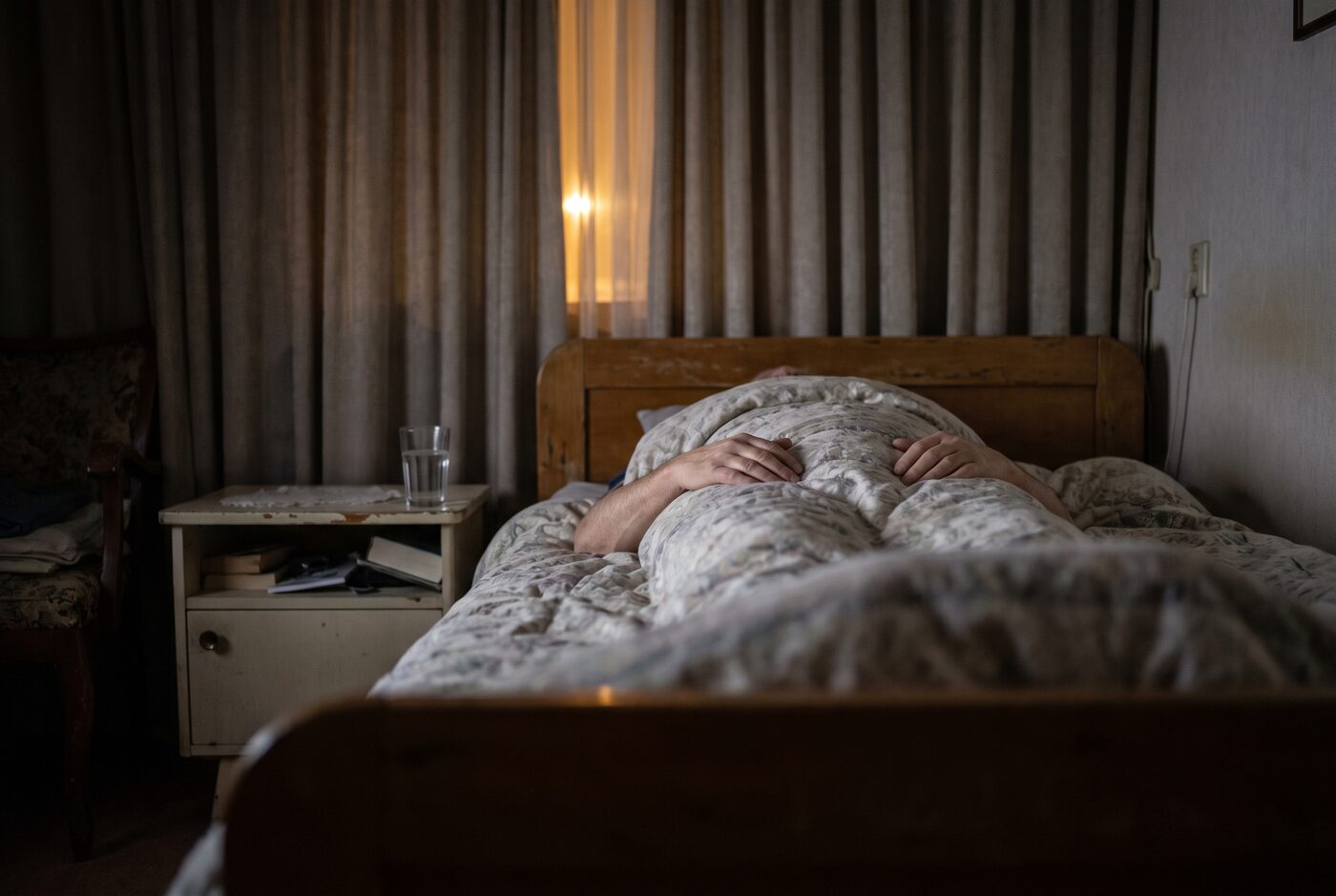 Iemand ligt 's nachts op zijn rug in bed met de handen op het dekbed