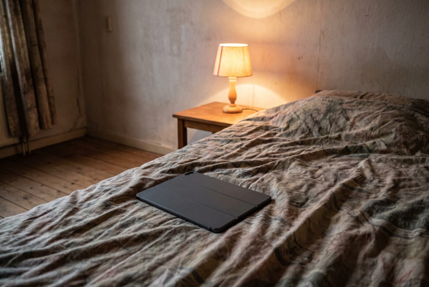 Een tablet ligt met het scherm naar beneden op een dekbed in een donkere slaapkamer