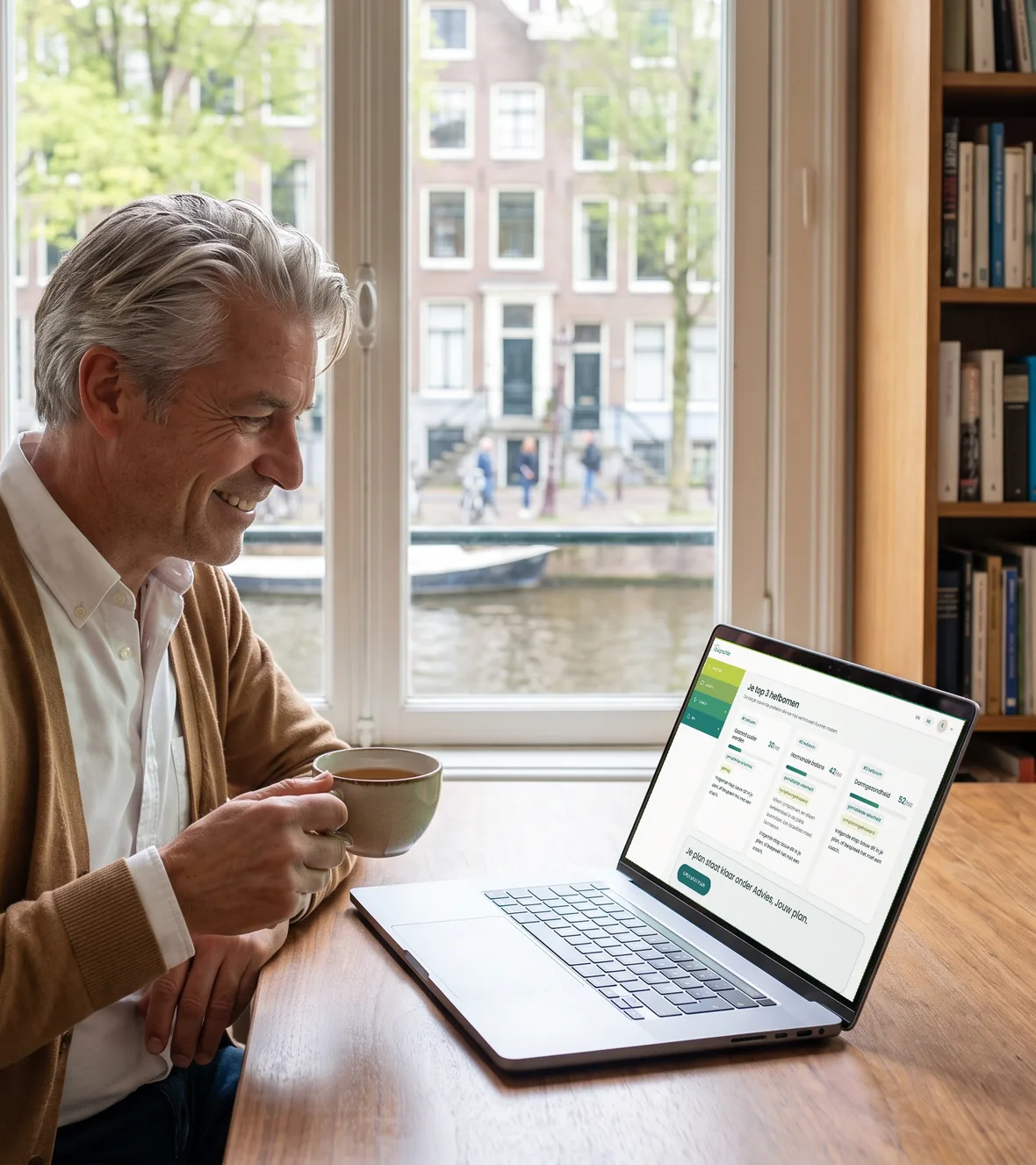 Een man van begin vijftig met zilvergrijs haar, in een wit overhemd en een camelkleurig vest, zit aan een bureau voor een raam aan een Amsterdamse gracht en kijkt glimlachend naar de laptop, met de analyseresultaten van de BioProfile-app op het scherm.